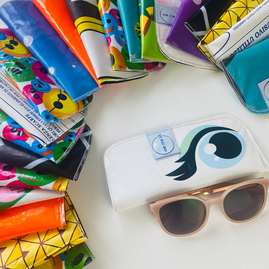 Colorful cases and a white wallet made from broken inflatables, with a logo on a white surface, with sunglasses in the foreground.