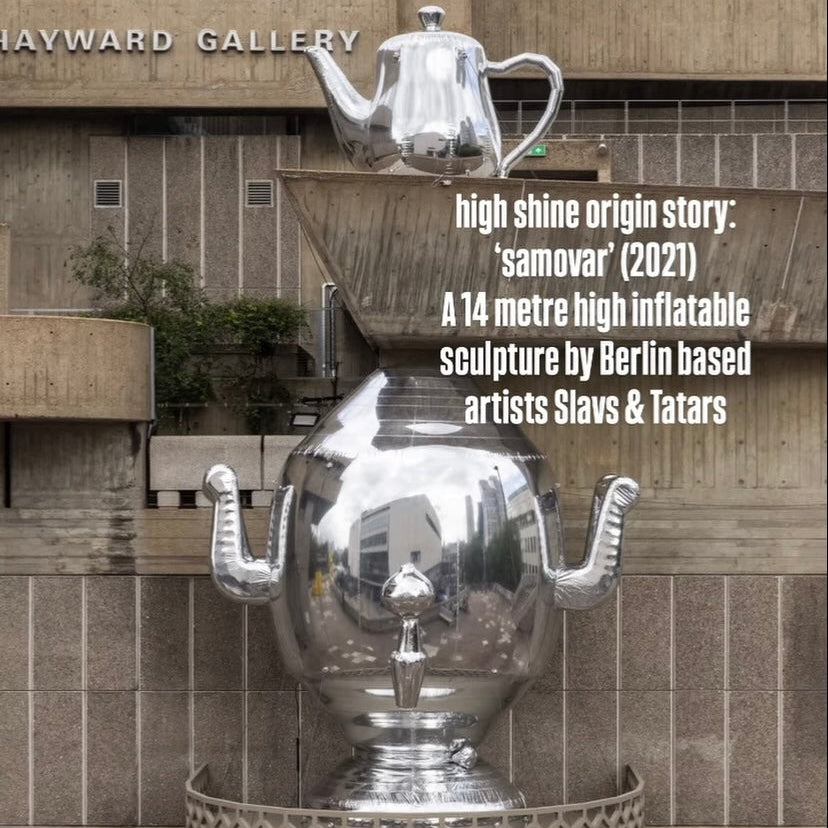 A large reflective silver sculpture resembling a teapot and teapot handle arrangement sits outdoors in front of a modern concrete building. White text on the right reads 'high shine origin story: "samovar" (2021) A 14 metre high inflatable sculpture by Berlin based artists Slavs & Tatars'.