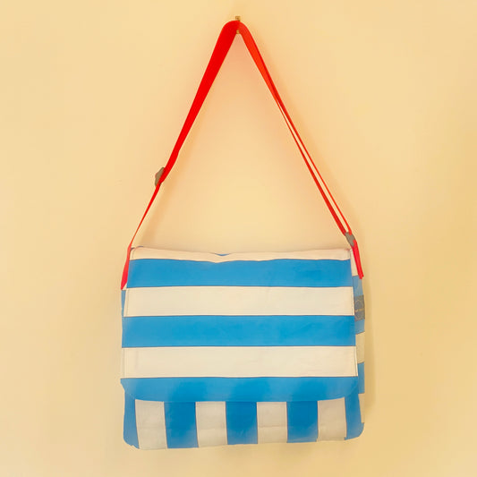 A blue and white striped fabric shoulder bag with a bright red strap, hanging against a plain beige wall.