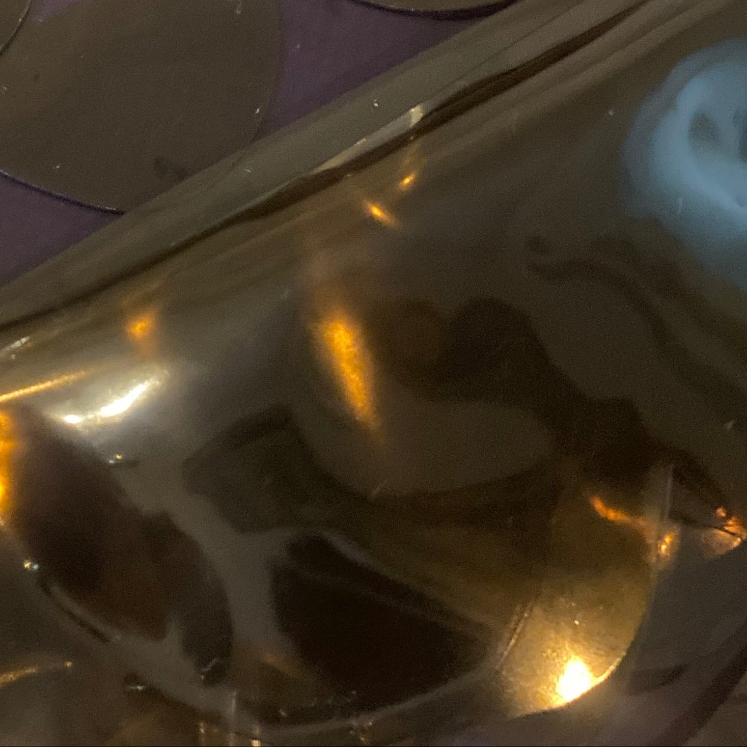 A close-up of a metallic gold surface with overlapping scalloped circular cutouts and reflective highlights, showing warm amber reflections and a faint purple cast in the background.